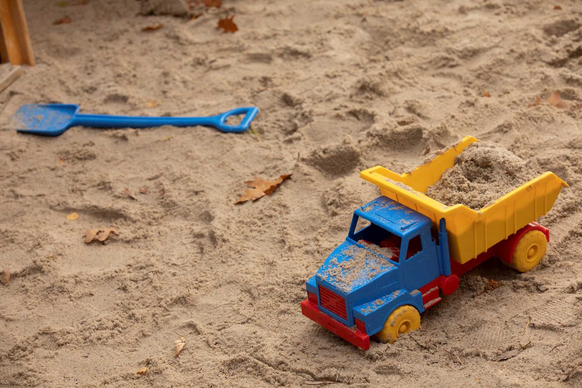 Legetøjslastbil og skovl, der ligger i sandkasse