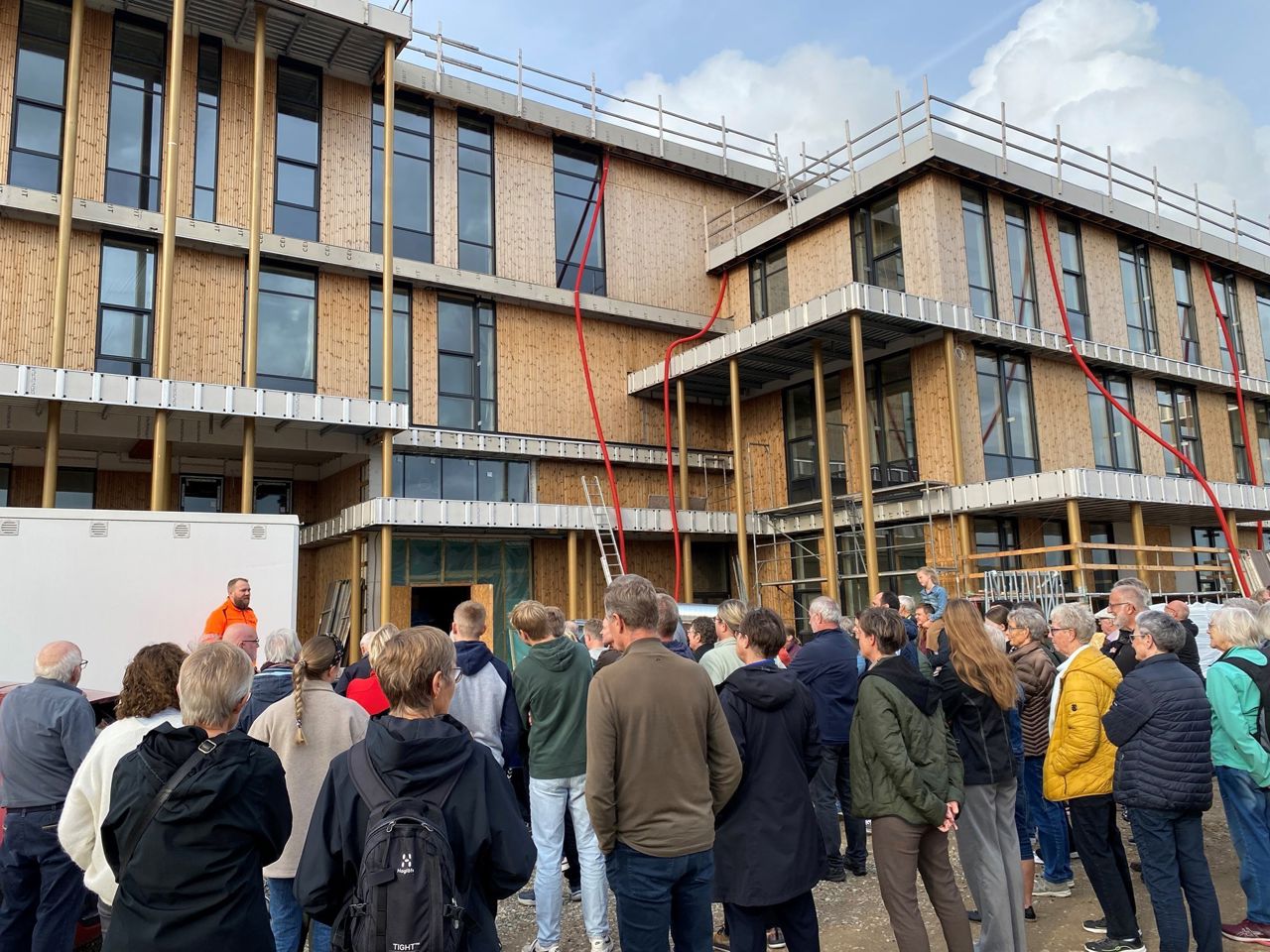 En gruppe voksne personer uden foran Lysningen Skole, der er under opførsel.